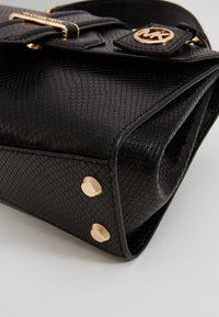 Svart texturerad handväska med ett reptilhudsmönster, guldbeläggningar och en magnetisk stängning med logotypdetalj.