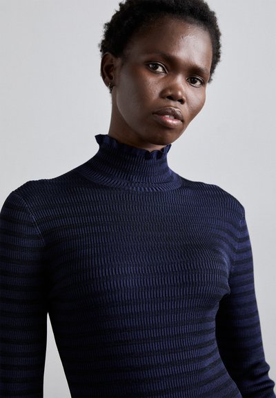 Navy ribbed turtleneck sweater with a textured finish and ruffled collar. Features a fitted silhouette and subtle vertical stripes.