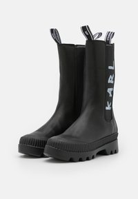 Stivali alla caviglia in pelle nera con lati elasticizzati, suole in gomma rigata e logo "KARL" sul lato. Texture liscia, design moderno.