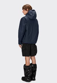 Marine vandtæt jakke med hætte, sorte cargo shorts og sorte blanke vandtætte støvler. Glat tekstur og minimalistisk design.