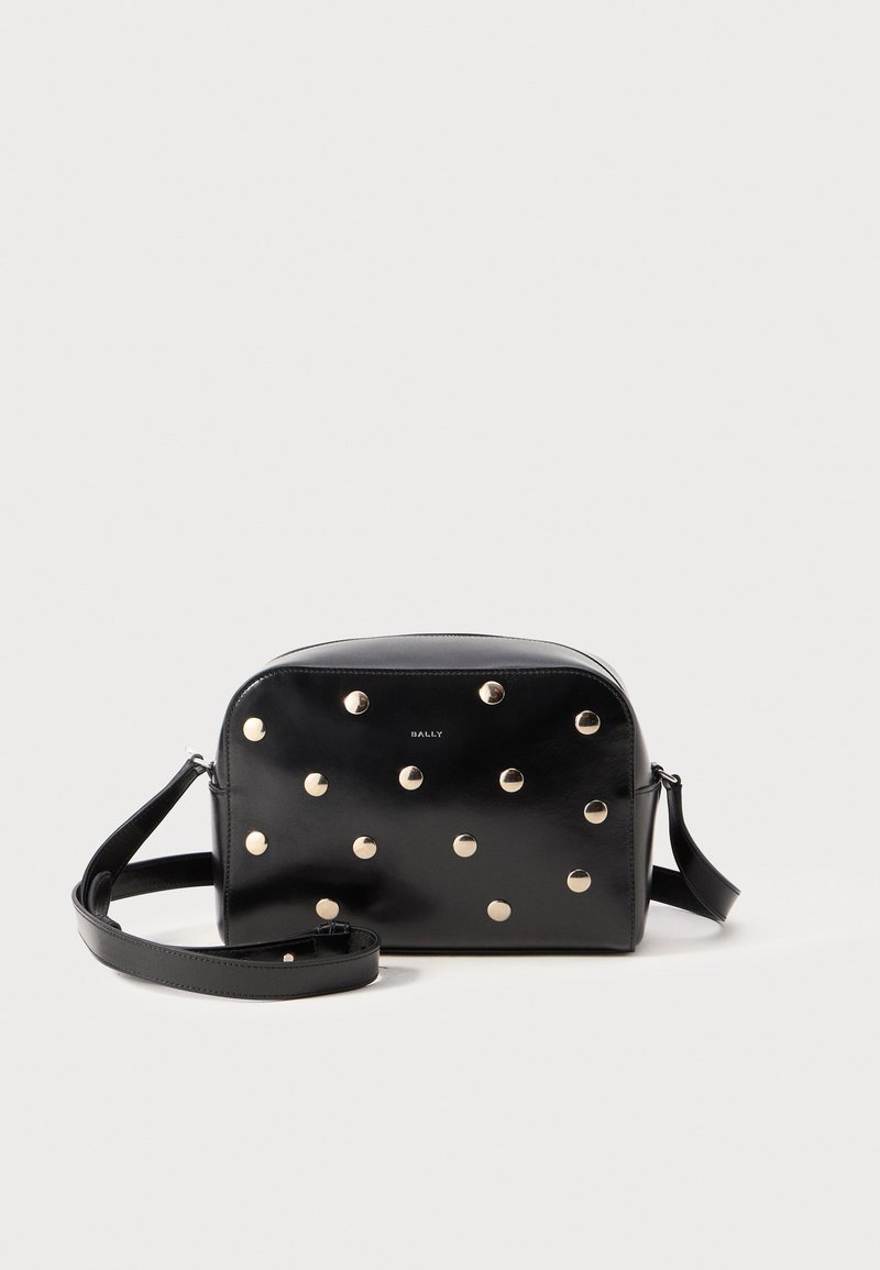 Černá kožená crossbody taška s kulatými zlatými hřebíky a nastavitelním popruhem. Kulatý tvar s hladkým povrchem a logem na přední straně.