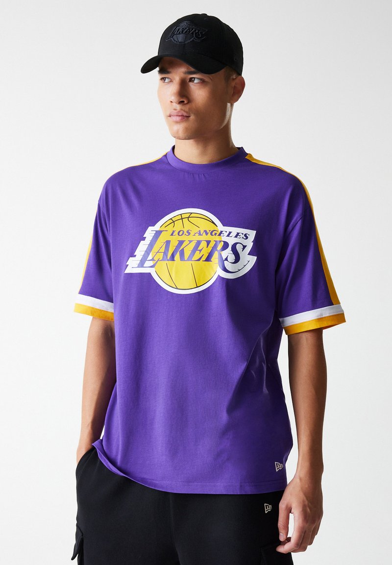 Lila t-shirt med kort ärm och gula detaljer, med en vit Los Angeles Lakers-logotyp och en basketgrafik. Tillverkad av bomull.
