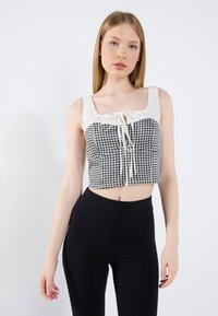 Top corto con un patrón de cuadros en blanco y negro, con un nudo en la parte delantera y tirantes anchos; combinado con leggings negros de canalé de cintura alta.