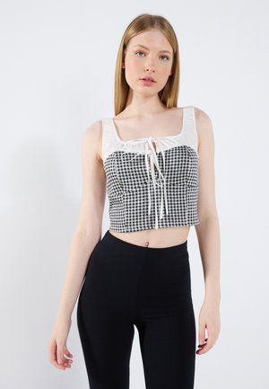 Top corto con un patrón de cuadros en blanco y negro, con un nudo en la parte delantera y tirantes anchos; combinado con leggings negros de canalé de cintura alta.