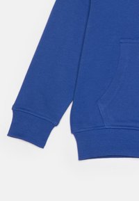 Felpa blu con polsini a costine e tasca frontale, realizzata in morbido tessuto testurizzato. Visibili dettagli delle cuciture.