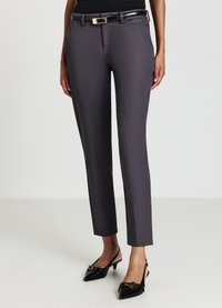 Pantalons gris ajustés avec une coupe slim, texture lisse et une ceinture noire brillante avec une boucle dorée. Portés avec des talons aiguilles noirs.