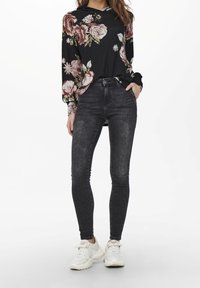 Haut noir à manches longues avec des fleurs roses et blanches, associé à un jean en denim noir ajusté et des baskets blanches. Tenue décontractée mettant en valeur le motif floral.