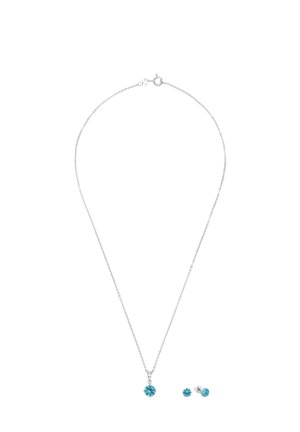 Collier chaîne en argent et boucles d'oreilles clous assorties avec pendentifs en pierres précieuses rondes bleues sur fond blanc.