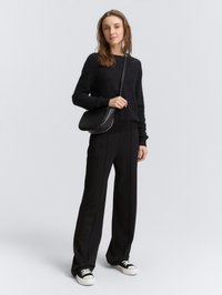 Cardigan nero a texture con scollo rotondo, abbinato a pantaloni neri a gamba larga con cuciture laterali. Completato con sneakers nere e una borsa a tracolla.