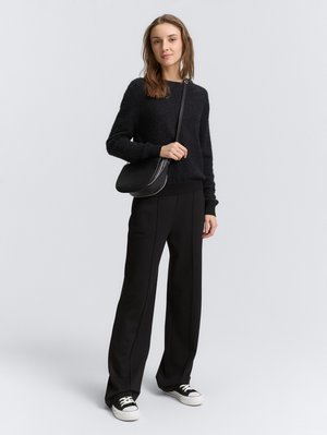 Cardigan nero a texture con scollo rotondo, abbinato a pantaloni neri a gamba larga con cuciture laterali. Completato con sneakers nere e una borsa a tracolla.