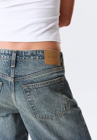 Τζιν από ανοιχτό μπλε ντένιμ με άνετη εφαρμογή, που διαθέτουν καφέ δερμάτινο ταμπελάκι με την επιγραφή "WEEKDAY" και διπλές πίσω τσέπες.