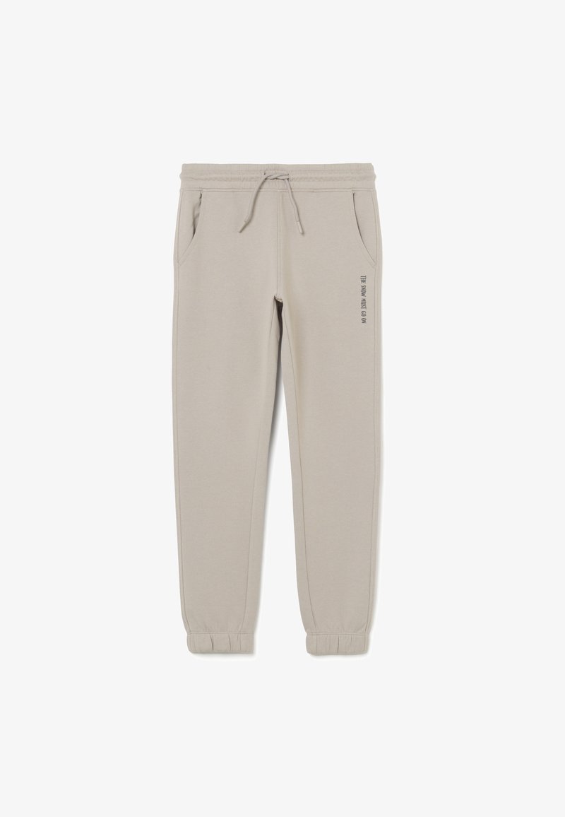 Pantalones jogger beige claro con cinturilla y puños elásticos, cordón, bolsillos laterales y la frase "LA NIEVE DEBE CONTINUAR" impresa en el muslo izquierdo.