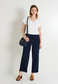 Haut blanc à manches courtes avec un décolleté festonné, associé à un pantalon large navy. Sandales à talons blocs marron et sac bandoulière navy.
