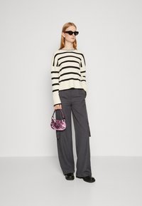 Pulover tricotat cu dungi negre și crem, pantaloni gri largi, și o geantă mică roz strălucitoare cu mânere din lanț, asortate cu ochelari de soare negri.