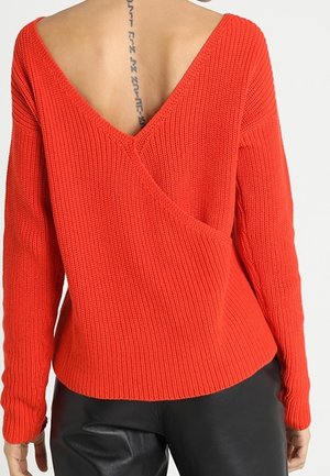 Maglione rosso lavorato a maglia con una profonda scollatura a V sul retro, maniche lunghe e un motivo texturizzato. Il design presenta un taglio asimmetrico all'orlo.