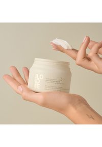 BONDINITY Diepe Herstelmasker in een lichte crème pot bevat een dikke, witte substantie. De tekst is ingedrukt, en een hand brengt het product uit de pot aan.