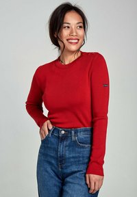Czerwony sweter prążkowany z okrągłym dekoltem i guzikami na ramionach, zestawiony z niebieskimi dżinsami z wysokim stanem.