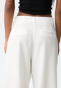 Witte wijde broek met een gladde, zachte textuur, voorzien van dubbele achterzakken en een platte tailleband. Geen zichtbare hardware of patronen.