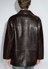 Braune Lederjacke mit glatter Textur, geradem Schnitt und großem Kragen. Sichtbare Nähte entlang der Nähte, Ansicht von hinten.