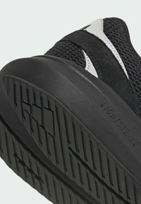 Czarny obuwie sportowe z teksturowaną siateczkową cholewką i czarną gumową podeszwą. Wyraźne logo "LIGHTSTRIKE" po bokach podkreśla design.