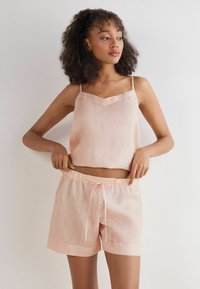 Světle růžový lněný crop top s tenkými ramínky a výstřihem do V, spárovaný s odpovídajícími šortkami na stažení s elastickým pasem.