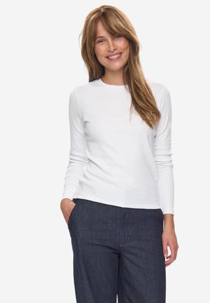 Weißes Langarmshirt mit Rundhalsausschnitt, kombiniert mit dunkelblauen Jeans, die einen lässigen Schnitt und ein einfaches Design aufweisen.