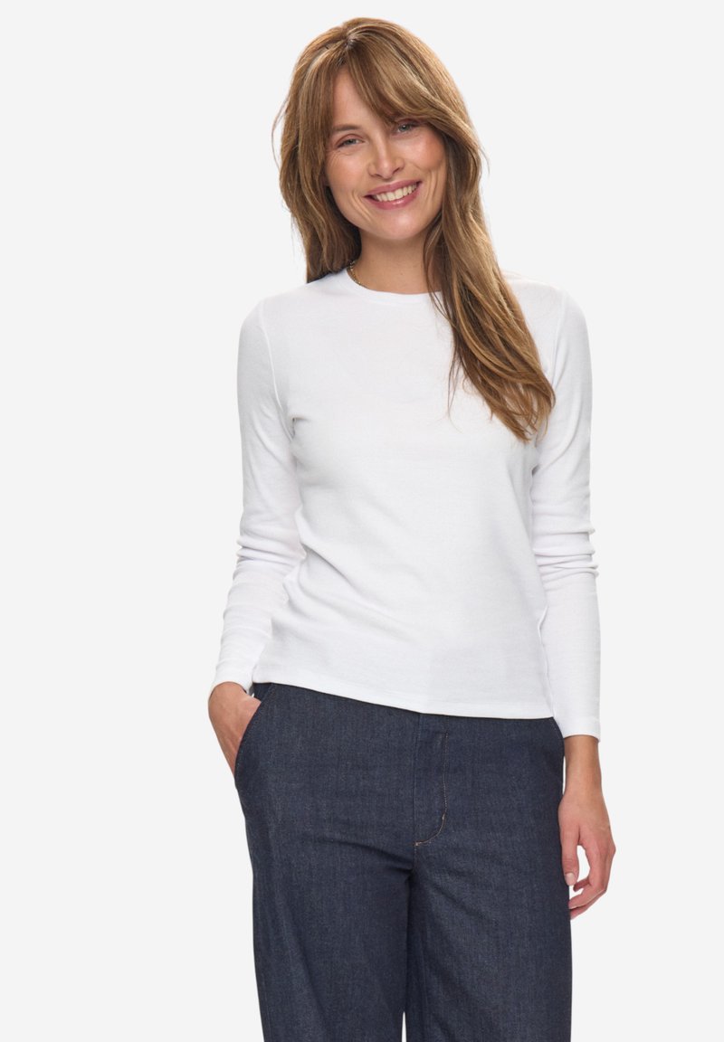 Weißes Langarmshirt mit Rundhalsausschnitt, kombiniert mit dunkelblauen Jeans, die einen lässigen Schnitt und ein einfaches Design aufweisen.