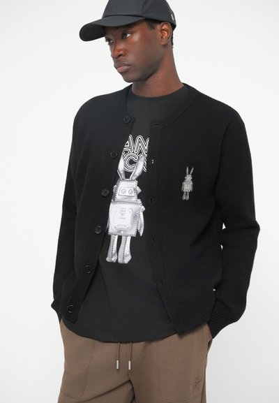 Black cardigan with a round neck, featuring button closure and ribbed cuffs, worn over a graphic black T-shirt with a rabbit design.
