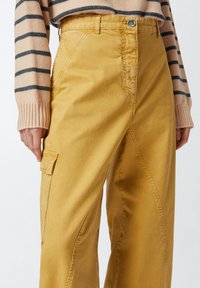 Žute pamučne cargo hlače s visokim strukom, s bočnim džepovima, zatvaračem i istaknutim šavovima duž nogu.
