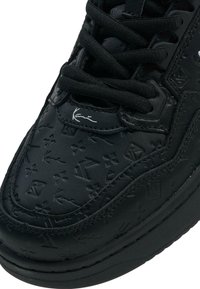 Fekete sneaker, domború mintázattal, vastag gumi talppal, fekete fűzőkkel és diszkrét logóval az oldalon. Textúrált bőrfelület.