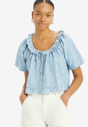 Light blue chambray blouse featuring a frilled neckline, short sleeves, floral embroidery, and a scalloped hem with button closure.