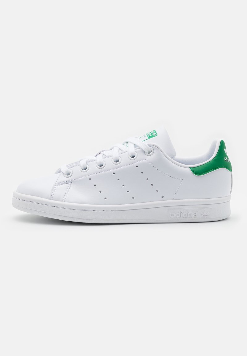 Zapatilla de cuero blanca con detalles en verde, diseño perforado en el lateral, puntera redonda, cierre con cordones y suela plana de goma. Marca en el talón.