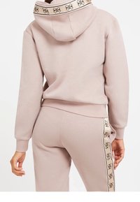 Sudadera de color rosa claro con cordón y ribete estampado. Pantalones deportivos a juego con una franja lateral con detalle de logotipo. Tela suave, ajuste relajado.