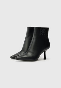 Bottines noires en cuir avec un bout pointu et un talon transparent fin. Présente le logo DKNY en relief sur le côté. Texture lisse.