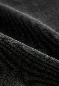 Gros plan sur un tissu noir plié avec une texture tissée en diagonale visible et des ombres douces mettant en valeur les contours de sa surface.