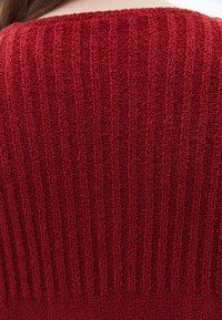 Röd stickad tröja med vertikal ribbad textur, rund halsringning och medelviktig tyg. Färgen är enhetlig utan synliga mönster.