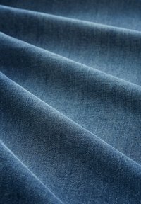 Gros plan d’un tissu denim bleu doux plié montrant une texture détaillée et un motif de tissage diagonal.