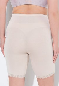 Shorts modelants beiges en tissu lisse, avec une coupe ajustée et une délicate dentelle au bas. Pas de coutures visibles.