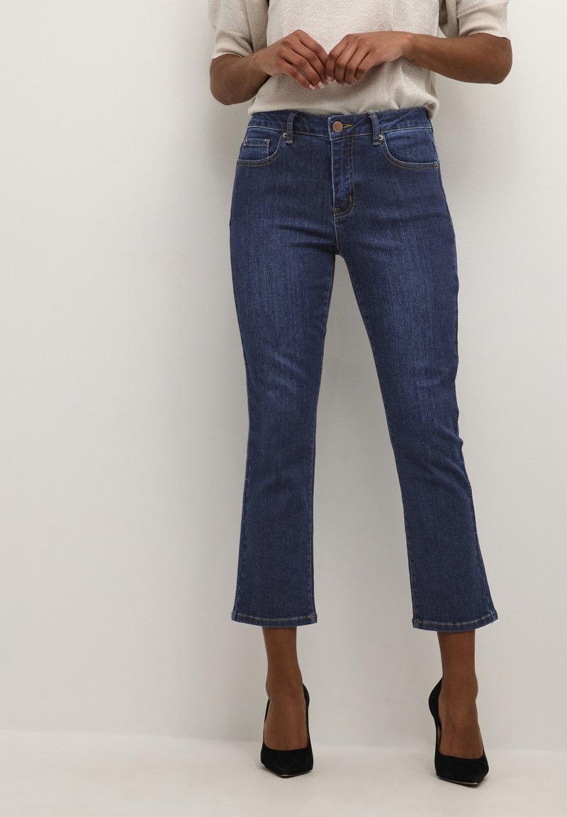 Mörkblå denimjeans med hög midja, utsvängd nederkant och subtila sömmar. Har en framknapp, dragkedja och klassisk femficksdesign.