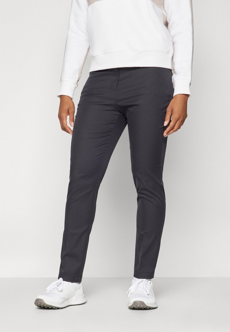 Σκούρο γκρι στενά παντελόνια κατασκευασμένα από απαλό ύφασμα, με επίπεδη μπροστινή όψη και πλαϊνές τσέπες, συνδυασμένα με λευκά αθλητικά παπούτσια.