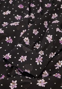 Zwarte stof met kleine witte stippen, versierd met verspreide paarse bloemen en gestructureerde zwarte cirkels. Zachte, gladde textuur met een vloeiende uitstraling.