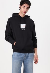 Felpa nera realizzata in misto cotone, con tasca frontale e dettagli grafici con strisce bianche e colorate. Vestibilità casual e polsini a coste.
