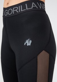 Black athletic leggings with a grey waistband and logo. Features mesh panels on the sides. Smooth texture with a snug fit.