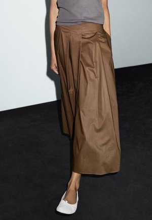 Brown, pleated maxi skirt with a smooth texture, featuring side pockets. Paired with white slip-on shoes. Simple gray top.