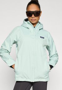 Αδιάβροχο μπουφάν ανοιχτού γαλάζιου χρώματος με κουκούλα, εμπρόσθιο φερμουάρ και πλαϊνές τσέπες. Διαθέτει ρυθμιζόμενα κορδόνια και λογότυπο στο στήθος.