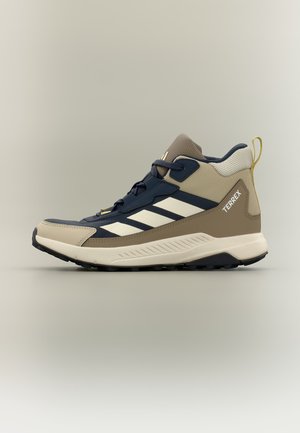 Beige und marineblauer Adidas Terrex Mid-Top Wanderschuh mit weißen Streifen, gepolstertem Knöchel, strukturierter Sohle und gelbem Fersenlaschen.