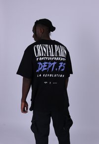 Černé oversized tričko s výrazným bíl�ým a modrým textem na zadní straně, které obsahuje "CRYSTAL PARIS" a "DEPT. 75".
