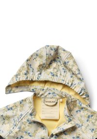 Chaqueta impermeable con estampado de flores en gris claro con un interior amarillo. Presenta una capucha con cordón, cierre de cremallera y botones a presión en el cuello.