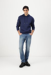 Navy hoodie with drawstrings and front pocket, paired with light blue jeans and black shoes. Simple design, casual look.