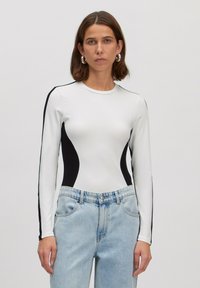 Witte lange mouwen bodysuit met zwarte zijkanten, ronde halslijn en rekbare stof. Gecombineerd met lichtgewassen denim broek.